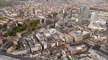 Modern ve tarihi binaların, yeşil alanların ve işlek caddelerin karışımından oluşan bir şehir manzarası. Ufuk çizgisi yüksek binalar ve kentsel kalkınmayı içeriyor.