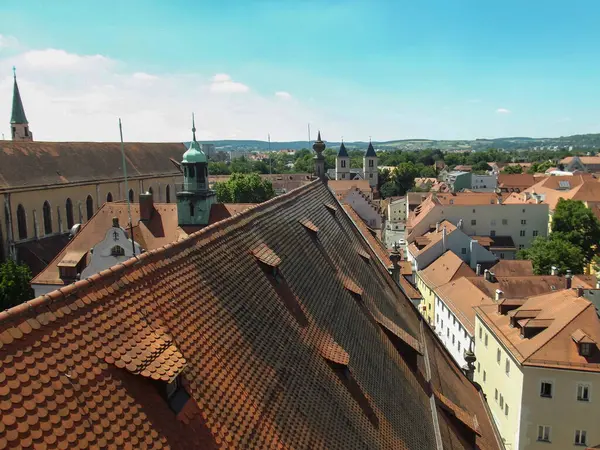 Geleneksel çatıların, kilise kulesinin ve açık mavi gökyüzünün altında yemyeşil yemyeşil bir zeminin olduğu panoramik bir manzara..