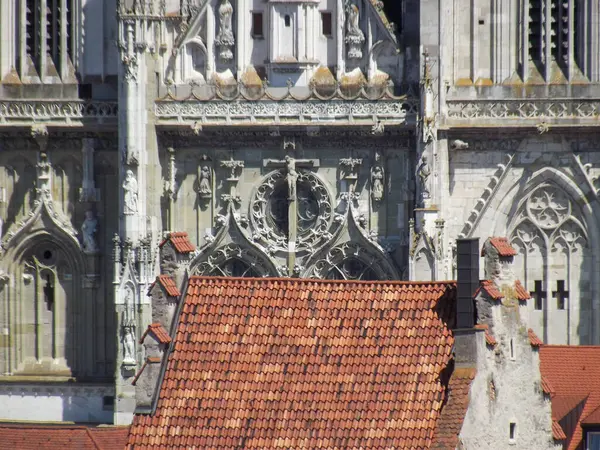 Detaylı taş oymaları ve kırmızı kiremitli çatısı olan karmaşık Gotik mimarinin yakın plan görüntüsü. Resim, heykeller ve dekoratif öğelerle bir katedral cephesinin dekoratif tasarımını sergiliyor..