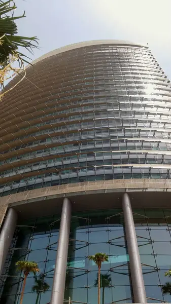 Birden fazla zemin ve eşsiz bir mimari tasarımı olan, cam cepheli, modern, eğri bir gökdelen. Bina palmiye ağaçlarıyla çevrili, güneşli bir gün yaşanıyor..