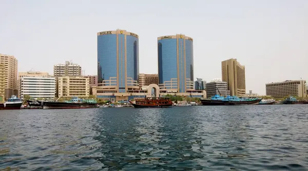 Rıhtım boyunca uzanan modern gökdelenlerin manzarası. Ön planda geleneksel ahşap tekneler var. Ufuk çizgisi çağdaş mimari ve kültürel öğelerin bir karışımını sergiliyor..