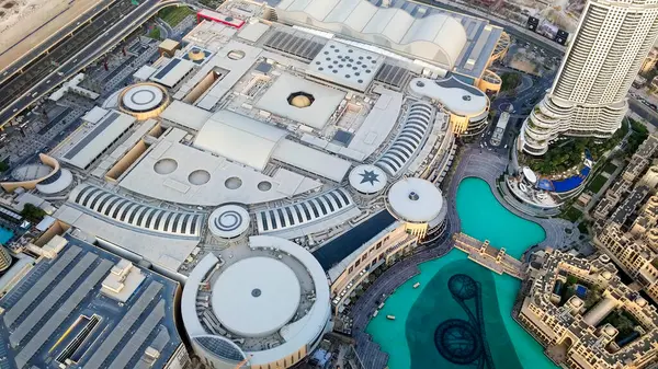 Su özellikleri ve yüksek binalarla çevrili, modern mimarisi olan büyük bir alışveriş merkezi kompleksinin havadan görünüşü. Düzen dairesel ve geometrik tasarımları içeriyor, lüks perakende alanları gösteriyor.