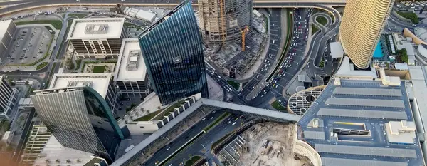 Gökdelenlerin, işlek yolların ve binaları birbirine bağlayan yaya köprüsünün yer aldığı modern şehir manzarası. Sahnede mimari ve şehir hayatının bir karışımı sergileniyor..