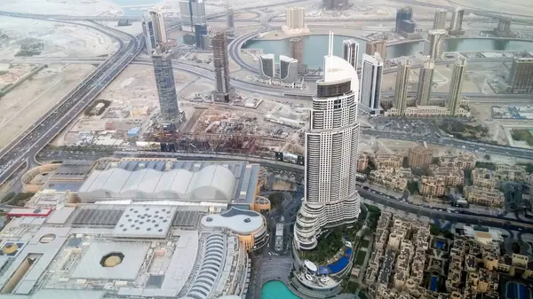 Yüksek binalar, yollar ve bir su yolu barındıran modern bir şehir manzarası. Önplanda, kentsel gelişim ve altyapı ile çevrili eşsiz bir tasarımı olan önemli bir gökdelen yer alıyor..