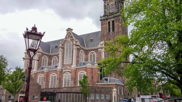 Ağaçlar ve sokak lambalarıyla çevrili uzun saat kulesi olan tarihi bir kilise binası. Gökyüzü bulutlu, sahneye dramatik bir atmosfer ekliyor..