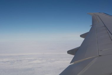 Bulutların üstündeki bir uçaktan gelen hava manzarası, açık mavi bir gökyüzü ve aşağıdaki geniş beyaz bulutları gösteriyor..