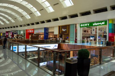 Çoklu perakende mağazaları, cam korkulukları ve parlak ışıklandırmaları olan modern bir alışveriş merkezi. Alışveriş merkezinin arka planında müşterilerin görebileceği geniş bir yerleşimi var..