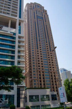 Diğer binalarla çevrili, eşsiz bir mimari tasarımı olan uzun, modern bir gökdelen. Yapıda cam ve beton karışımı ve tabanda belirgin bir giriş var..