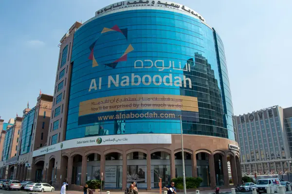 Ön cephesinde Al Naboodah için büyük bir reklam olan modern cam bir bina. Bina, çağdaş mimarinin sergilendiği kentsel bir alanda yer alıyor. Yakın yapılar arasında bir banka ve lüks perakende mağazaları yer alıyor.