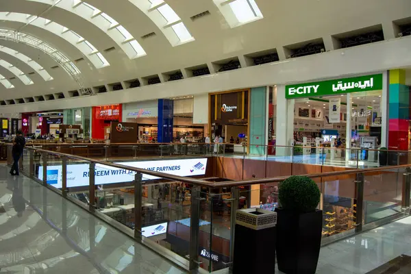 Çoklu perakende mağazaları, cam korkulukları ve parlak ışıklandırmaları olan modern bir alışveriş merkezi. Alışveriş merkezinin arka planında müşterilerin görebileceği geniş bir yerleşimi var..