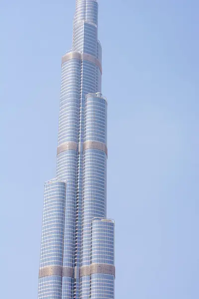 Parlak cam bir cepheli modern bir gökdelenin yakın görüntüsü, eşsiz mimari tasarımını ve açık mavi gökyüzüne karşı birden fazla katmanı sergiliyor..