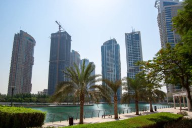 Rıhtım boyunca uzanan modern gökdelenlerin manzarası. Önünde palmiye ağaçları ve açık mavi bir gökyüzü var..
