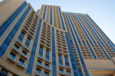 Çok sayıda cam pencere ve balkon barındıran, eşsiz kıvrımlı bir tasarımı olan modern bir gökdelen. Yapıda, çağdaş mimariyi yansıtan bej ve mavi renklerin bir karışımı yer alıyor..