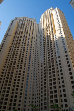 Çok sayıda pencere ve balkon barındıran modern mimari tasarıma sahip uzun bir yerleşim yeri. Bina açık mavi gökyüzüne karşı kurulmuş, yüksekliği ve yapısı gözler önüne seriliyor..