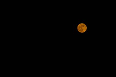 Parlak turuncu bir dolunay karanlık bir gece gökyüzüne karşı durgun ve büyüleyici bir atmosfer yaratıyor..