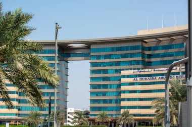 Merkezinde büyük bir kemer olan eşsiz bir mimari tasarımı olan modern bir bina. Ön cephe, mavi gökyüzünü yansıtan cam ve betondan yapılmıştır. Palmiye ağaçları ön planda görünür, tropikal bir hava katar..