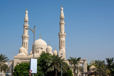 Uzun minareler ve palmiye ağaçları ve açık mavi gökyüzü ile çevrili büyük bir kubbenin yer aldığı güzel bir cami..
