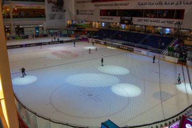 Kapalı bir buz pateni pistinde buz üstünde kayan patenciler. Pist, yüzeyi aydınlatan büyük spot ışıklarıyla iyi ışıklandırılmış. Seyirciler tribünlerde görülebilir ve pistte reklamlar sergilenebilir..