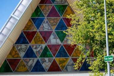 Geometrik desenleri ve dini figürleri barındıran renkli bir vitrin. Yeşillik zeminine kurulmuş ve şehir merkezini gösteren bir tabela..