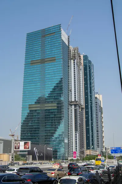 Yansıtıcı cam cepheli modern bir gökdelen, yapım aşamasında, diğer yüksek binalar ve kentsel bir ortamda yoğun trafik ile çevrili..