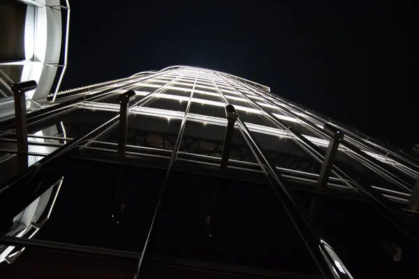 Geceleri uzun, aydınlık bir gökdelenin alçak açılı görüntüsü, karanlık gökyüzüne karşı cam cephesini ve mimari detaylarını gözler önüne seriyor..