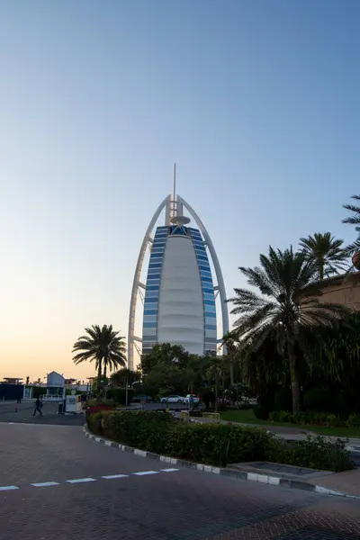 Günbatımında berrak bir gökyüzüne karşı seyreden yelkenliyi andıran modern bir mimari yapı. Önlerinde hurma ağaçları ve bahçeler vardır. Binaya doğru da yol alırlar..