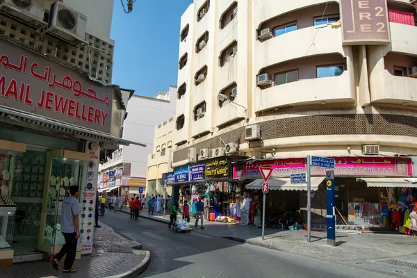 Orta Doğu 'da hareketli bir sokak sahnesi, renkli tabelalı dükkanlar, yaya yürüyüşleri ve geleneksel ve modern mimarinin bir karışımı. Atmosfer, çeşitli mağazalar ve günlük faaliyetlerle meşgul insanlarla dolu..