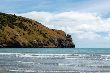 Kıyı manzaralı bir manzara kayalık bir uçurum, yuvarlanan tepeler ve parçalı bulutlu bir gökyüzünün altında kıyıya vuran nazik dalgalar..
