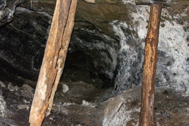 Tahta destekli bir yeraltı maden kuyusu kayalık duvarlar ve yerin derinliklerine açılan karanlık bir tünel gösteriyor..