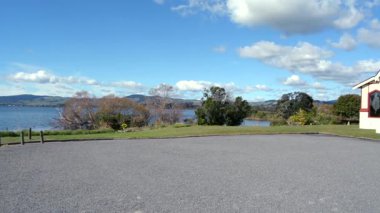 Kırmızı ve beyaz mimarisi olan tarihi bir binanın manzarası sakin bir gölün arka planına ve parçalı bulutlu bir gökyüzünün altında yuvarlanan tepelere karşı kurulmuş..