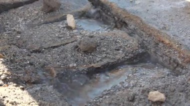 Boşluklardan akan suyla çatlamış kaldırımın yakın çekim görüntüsü toprak ve küçük taşların karışımını ortaya çıkarıyor. Olay yeri aşınma ya da su hasarı olduğunu gösteriyor..