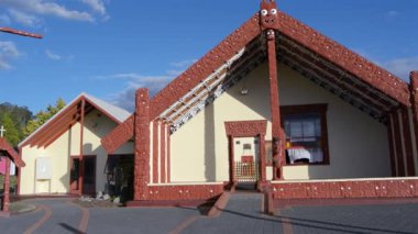 Geleneksel bir Mori toplantı evi (Wharenui), karmaşık oymalar ve kendine özgü çatı tasarımı ile mavi gökyüzüne karşı kurulur. Binada kırmızı ve beyaz renkler yer alıyor, kültürel sanatlar sergileniyor.