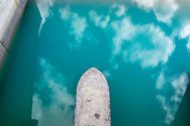 Teknenin pruvasının turkuaz su üzerindeki hava manzarası bulutları yansıtıyor..