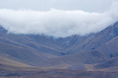 Bulutlarla kaplanmış dağların manzaralı manzarası yuvarlanan tepeler ve soluk renk paleti ile dramatik bir manzara sergiliyor. Ortam sakin ve huzurlu. Doğa aşıkları için ideal..