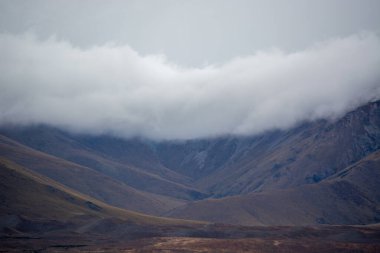 Yoğun bulutlarla kaplanmış dağların olduğu dramatik bir manzara karamsar bir atmosfer yaratıyor. Arazi, uzak ve el değmemiş bir çöle işaret eden toprak tonları ile engebelidir..