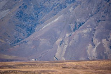 Kuru, kayalık yamaçları ve seyrek bitki örtüsüyle engebeli dağları barındıran engin bir manzara. Arazi toprak tonları ve izolasyon hissi ile karakterize edilir, sakin ama sert bir çevreyi çağrıştırır..