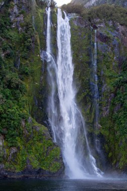 Bereketli yeşilliklerle çevrili kayalık bir uçurumdan şelalenin şelalesi düşüyor. Su aşağıdaki sakin bir havuza güçlü bir şekilde akar ve sisli bir atmosfer yaratır..
