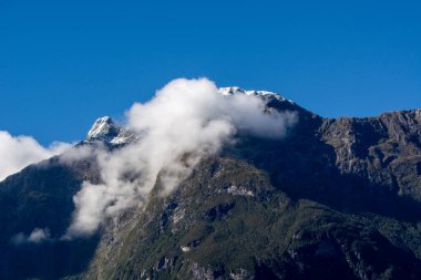 Karla kaplı tepeleriyle görkemli bir dağ manzarası kısmen bulutlarla kaplı berrak mavi bir gökyüzüne karşı..