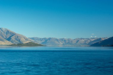 Berrak mavi gökyüzünün altında görkemli dağlarla çevrili sakin bir göle sahip sakin bir manzara. Su dağları yansıtıyor, sakin bir manzara yaratıyor..