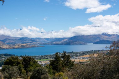 Dağlarla çevrili sakin bir göl manzarası ve bulutlu bir gökyüzünün altında yemyeşil bir yer..