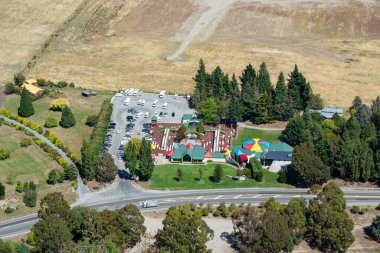 Renkli şemsiyeler ve bir otoparkın yer aldığı yeşilliklerle çevrili bir eğlence merkezinin havadan görüntüsü. Yakın tarlalar ve dolambaçlı bir yol görülebilir.