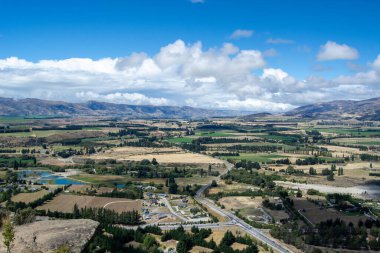 Parçalı bulutlu bir gökyüzünün altındaki dağlarla çevrili yemyeşil bir vadinin panoramik görüntüsü. Manzara, dolambaçlı bir nehir ve doğanın güzelliğini gözler önüne seren ağaçlar içerir..
