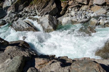 Büyük kayaların üzerinden akan ve köpüklü su oluşturan akan bir nehrin yakın çekim görüntüsü. Sahne kayalık bir arazide suyun doğal güzelliğini ve gücünü yakalar..