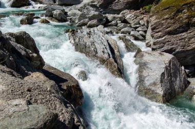 Kayalık arazide akan akıntılı bir nehrin manzarası, büyük taş ve kayaların üzerinden dökülen turkuaz su..