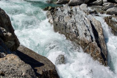 Kayalık arazide çağlayan suyun beyaz köpük ve su sıçrattığı yakın çekim görüntüsü. Sahne, suyun dinamik hareketini doğal bir ortamda yakalıyor ve pürüzsüz su ile sert taşlar arasındaki zıtlığı vurguluyor..