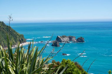 Bereketli yeşillik çerçeveli kayalık adalar ve turkuaz sulardan oluşan manzaralı bir kıyı manzarası. Gökyüzü birkaç bulutla berrak, sakin bir atmosfer yaratıyor..