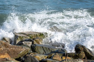 Dalgalar kayalık kıyı şeridine çarpıyor, sıçramalar ve köpükler yaratıyor. Sahne, su ve kayalar arasındaki dinamik etkileşimi yakalar ve doğanın gücünü gösterir..