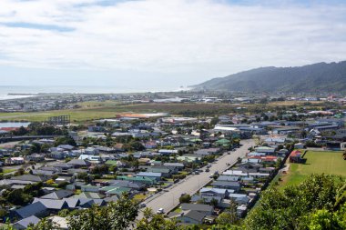 Tepeler ve okyanusla çevrili, yerleşim evleri ve yeşil tarlaların karışımından oluşan bir sahil kasabasının havadan görünüşü..