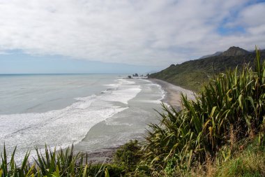 Kıyı şeridinin manzarası. Hafif dalgalar kıyıya vuruyor. Etrafı yemyeşil ve dağlarla çevrili..