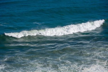 Kıyıya çarpan okyanus dalgalarının hava görüntüsü canlı mavi su ve beyaz köpüğü gösteriyor..